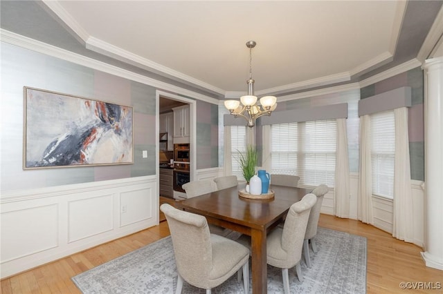 dining space featuring ornamental molding, light wood-style floors, wainscoting, a chandelier, and ornate columns