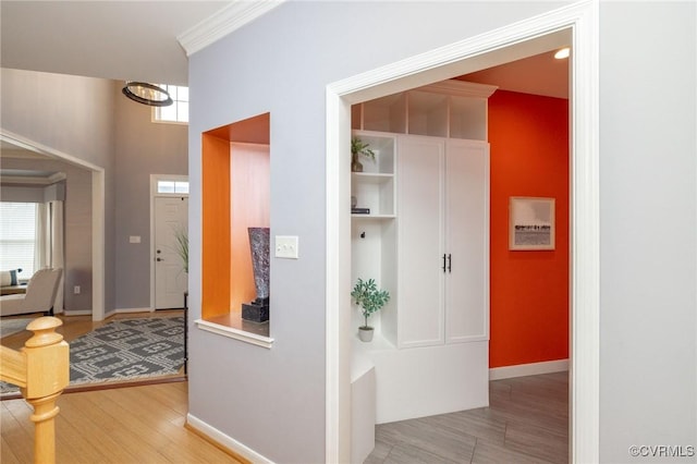 hallway featuring baseboards, light wood-style floors, and ornamental molding