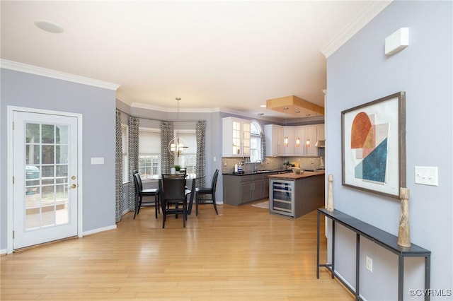 dining area featuring light wood-style flooring, beverage cooler, baseboards, and ornamental molding