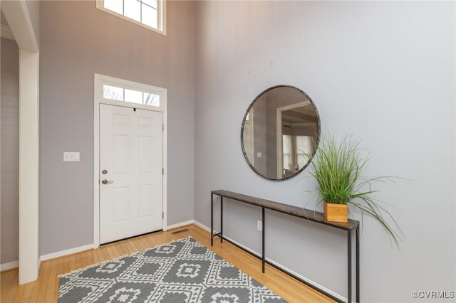 entryway with baseboards, wood finished floors, and a towering ceiling