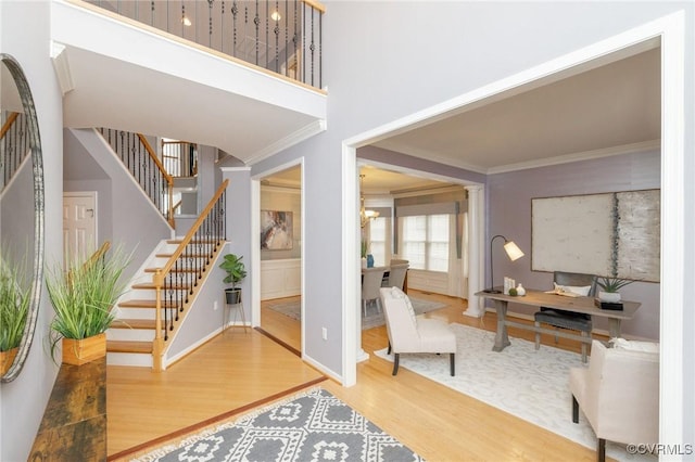 entrance foyer featuring stairs, ornamental molding, a high ceiling, an inviting chandelier, and wood finished floors