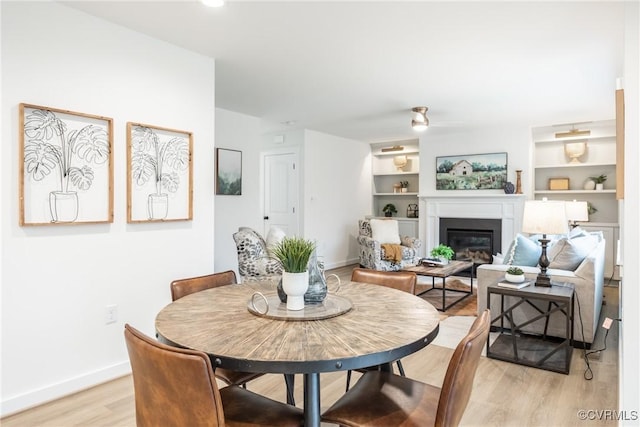 dining area featuring ceiling fan, baseboards, built in features, light wood-style flooring, and a glass covered fireplace