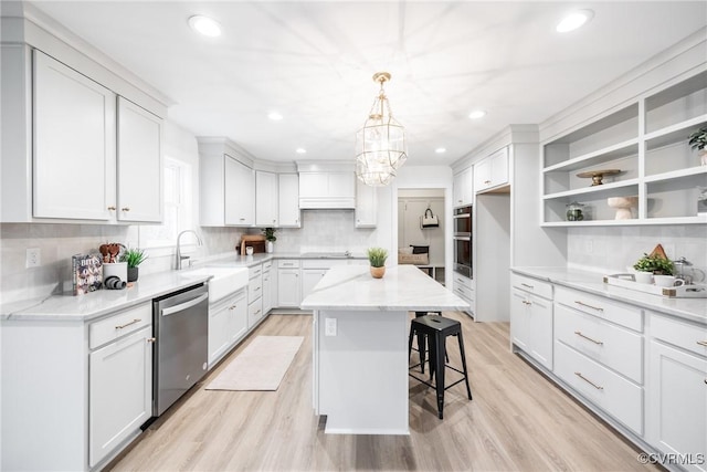 kitchen with light wood-style flooring, a sink, tasteful backsplash, a kitchen island, and appliances with stainless steel finishes