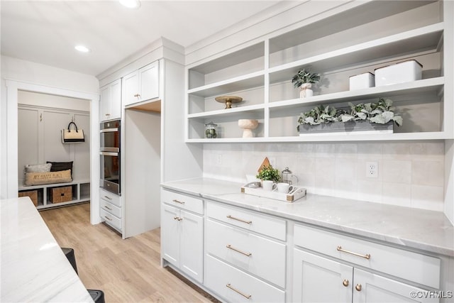 kitchen featuring open shelves, light stone counters, light wood-style floors, and white cabinets