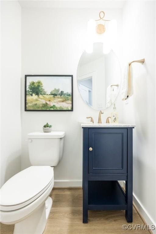 bathroom with vanity, toilet, wood finished floors, and baseboards