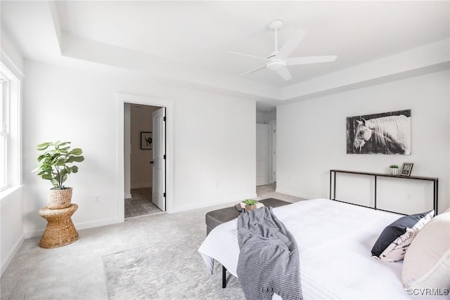 bedroom with a raised ceiling, multiple windows, baseboards, and light carpet