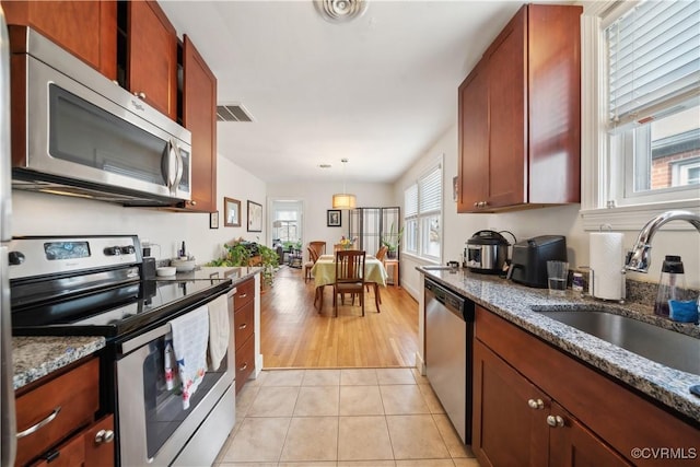 kitchen with visible vents, dark stone countertops, a sink, stainless steel appliances, and light tile patterned floors