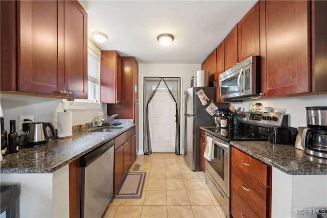 kitchen with dark stone countertops, light tile patterned floors, appliances with stainless steel finishes, and a sink