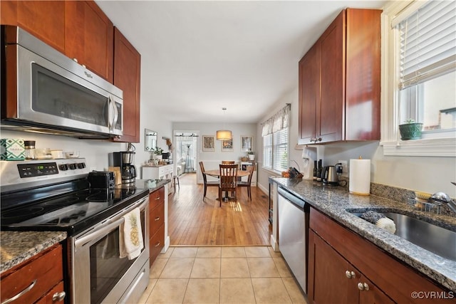 kitchen featuring dark stone counters, light tile patterned flooring, a sink, appliances with stainless steel finishes, and pendant lighting