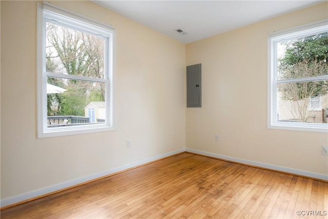 unfurnished room with electric panel, visible vents, light wood finished floors, and baseboards