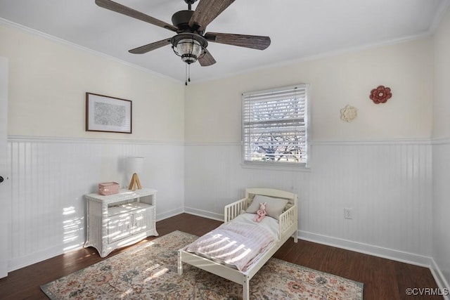 bedroom with crown molding, wood finished floors, and wainscoting