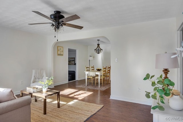 living area with baseboards, arched walkways, wood finished floors, and a ceiling fan