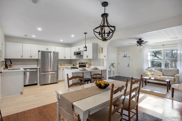 dining area featuring light wood-style flooring, a ceiling fan, recessed lighting, arched walkways, and baseboards