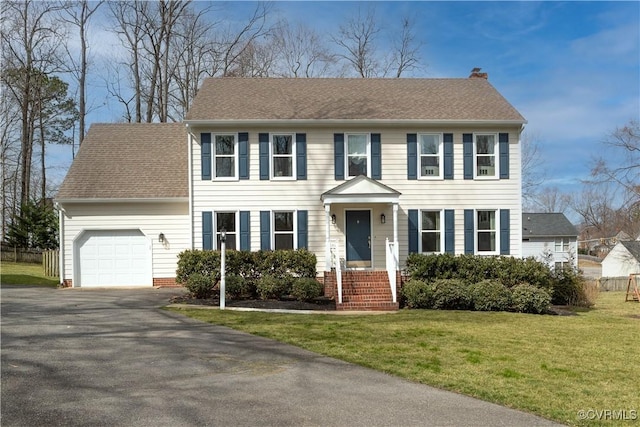 colonial home with a shingled roof, a front lawn, aphalt driveway, a chimney, and a garage