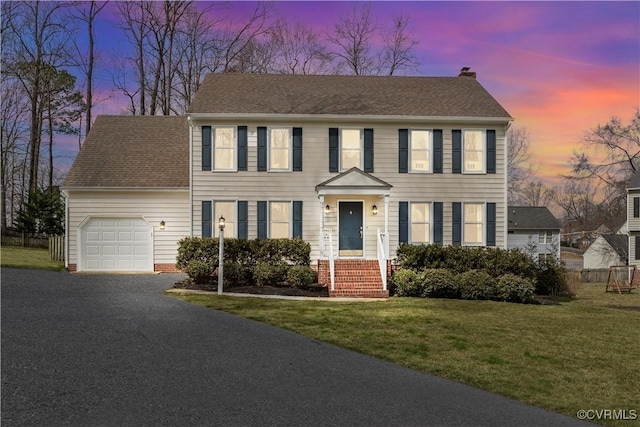 colonial inspired home with a lawn, driveway, roof with shingles, a garage, and a chimney