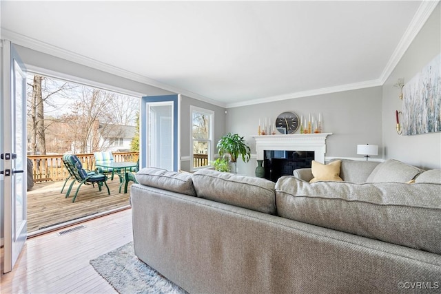 living area with crown molding, a fireplace, visible vents, and wood-type flooring