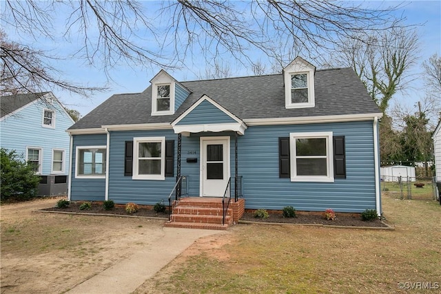 cape cod home featuring roof with shingles, a front lawn, and fence