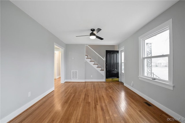 unfurnished living room with stairs, light wood-style flooring, baseboards, and visible vents