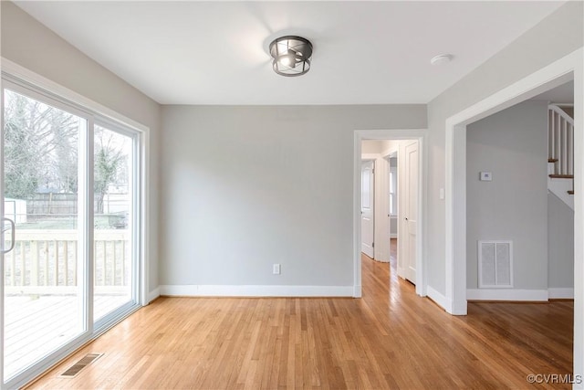 empty room with stairs, baseboards, visible vents, and light wood-type flooring