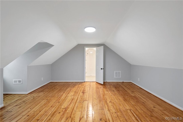 additional living space featuring light wood finished floors, visible vents, baseboards, and vaulted ceiling