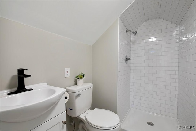 full bath featuring toilet, tiled shower, vanity, and vaulted ceiling