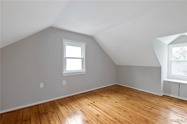 additional living space featuring vaulted ceiling, light wood-style flooring, plenty of natural light, and baseboards