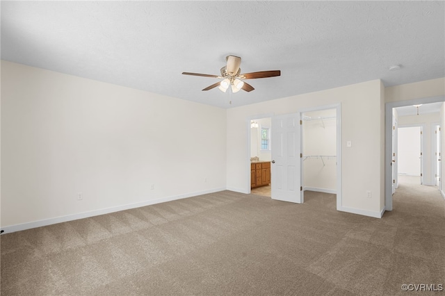 unfurnished bedroom with a walk in closet, a textured ceiling, a closet, baseboards, and light colored carpet