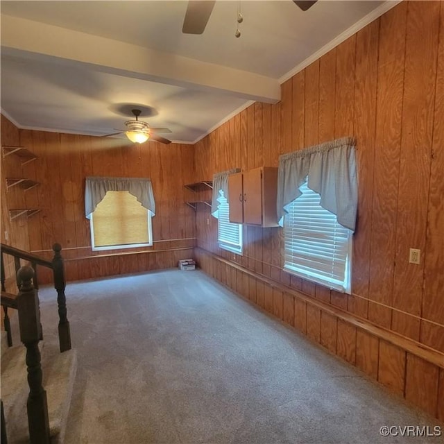 carpeted empty room with beamed ceiling, wooden walls, ornamental molding, and a ceiling fan