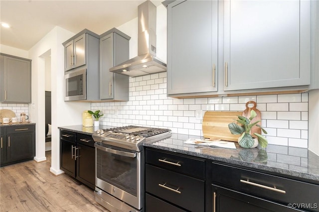 8160 Lyman Ct, Mechanicsville, VA 23116 - kitchen with stainless steel appliances, wall chimney range hood, dark stone countertops, light wood finished floors, and decorative backsplash