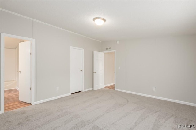 unfurnished bedroom featuring carpet flooring, ensuite bath, baseboards, and ornamental molding