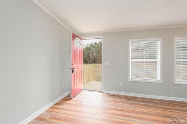 foyer with light wood finished floors, crown molding, and baseboards