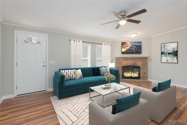 living area with a stone fireplace, crown molding, wood finished floors, and ceiling fan