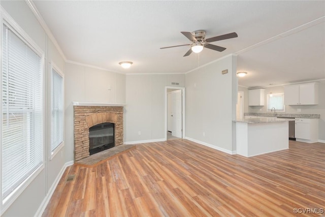 unfurnished living room featuring a stone fireplace, light wood-style flooring, crown molding, and ceiling fan