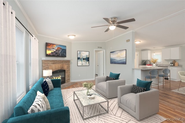 living room with visible vents, ornamental molding, a stone fireplace, light wood-style floors, and a ceiling fan