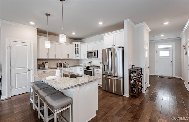 kitchen with dark wood finished floors, an island with sink, ornamental molding, stainless steel appliances, and a sink