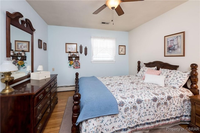 bedroom featuring a baseboard heating unit, visible vents, wood finished floors, and a ceiling fan