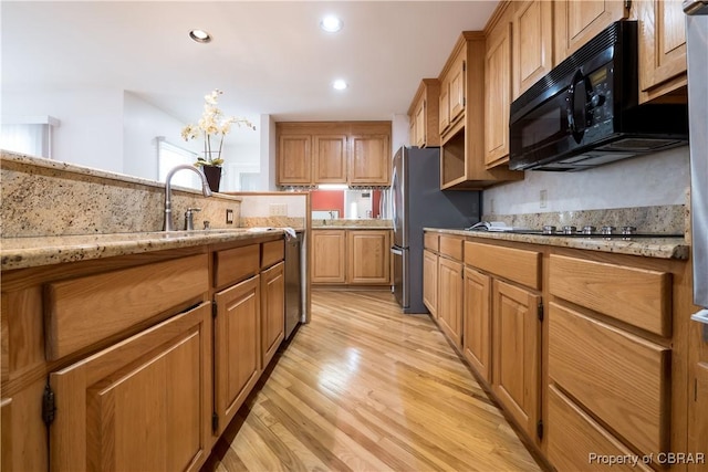 kitchen with light stone countertops, light wood finished floors, recessed lighting, black appliances, and a chandelier
