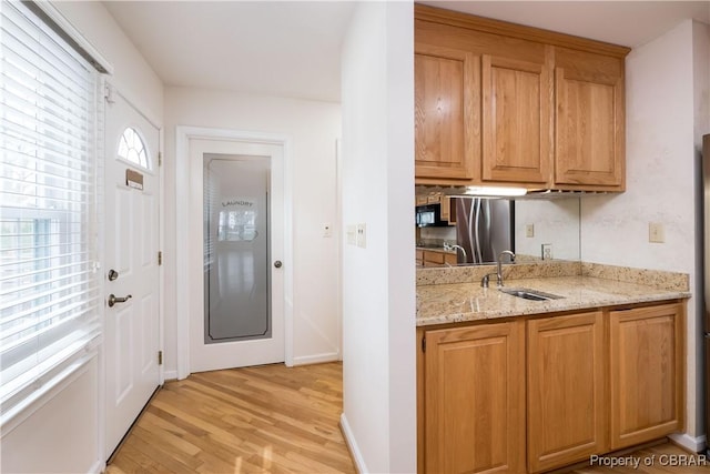 kitchen featuring baseboards, light wood-type flooring, light stone counters, freestanding refrigerator, and a sink