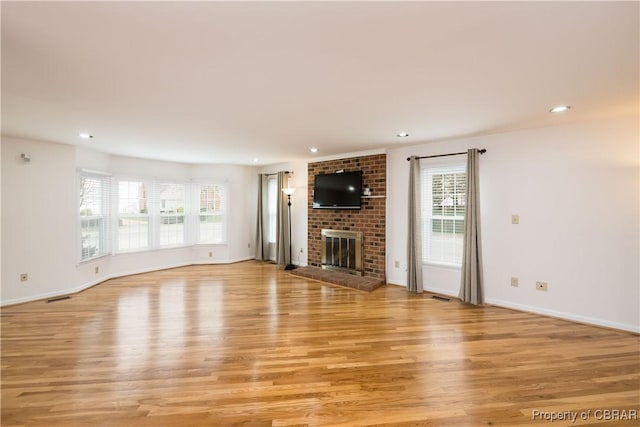 unfurnished living room featuring visible vents, plenty of natural light, a brick fireplace, and light wood-style floors