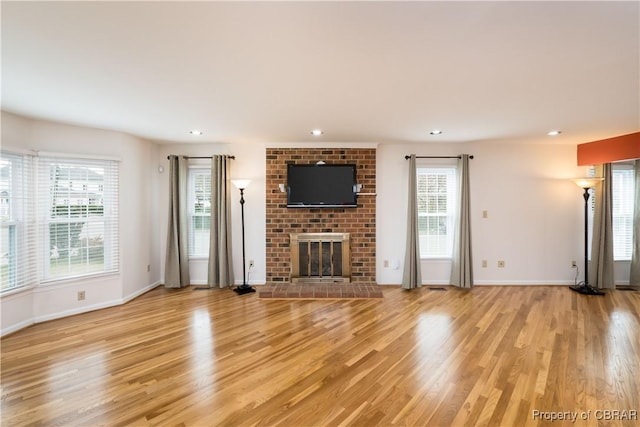 unfurnished living room featuring a healthy amount of sunlight, a brick fireplace, and light wood-type flooring