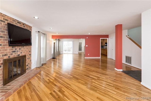 unfurnished living room featuring baseboards, visible vents, recessed lighting, a brick fireplace, and light wood-type flooring