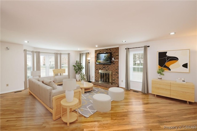 living room with plenty of natural light, recessed lighting, a brick fireplace, and light wood-type flooring