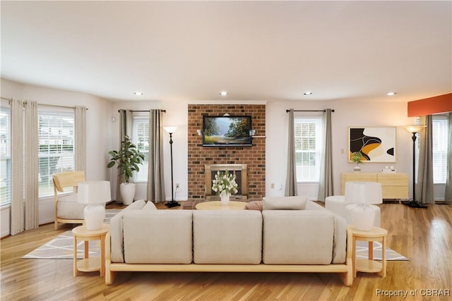 living room featuring plenty of natural light, a brick fireplace, and light wood-style floors