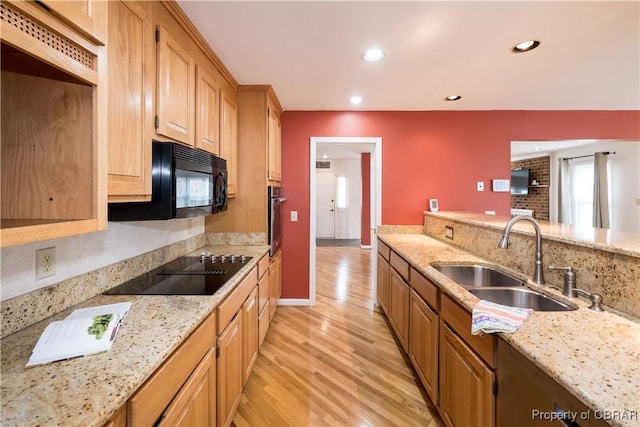 kitchen featuring a sink, light wood-type flooring, light stone counters, and black appliances