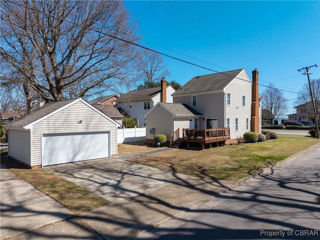 view of front of house featuring an outbuilding, a front lawn, a detached garage, fence, and a wooden deck