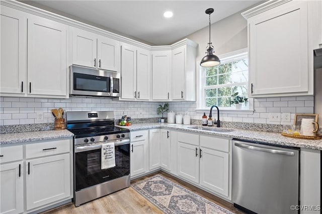 kitchen featuring backsplash, stainless steel appliances, light wood-style floors, white cabinetry, and a sink