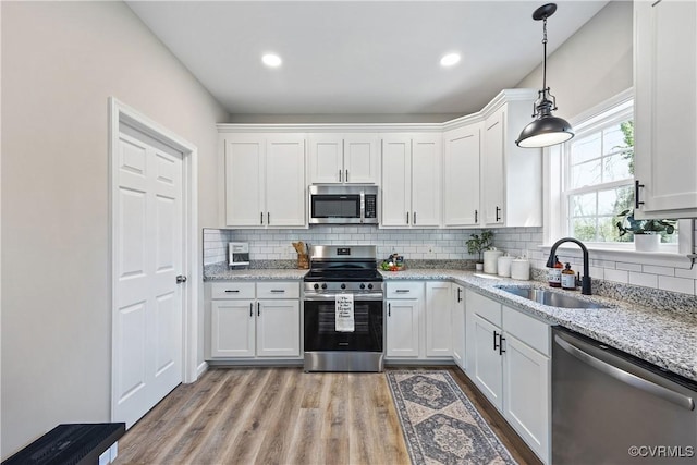 kitchen with a sink, backsplash, white cabinetry, stainless steel appliances, and light wood finished floors