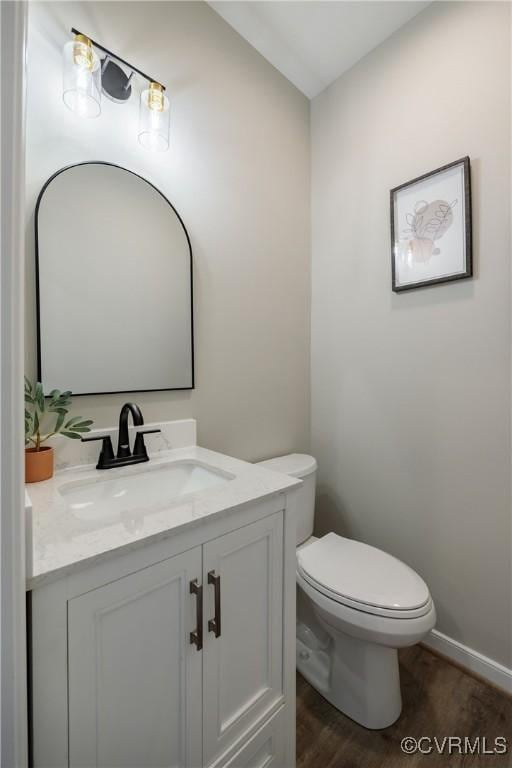 half bathroom featuring baseboards, toilet, wood finished floors, and vanity