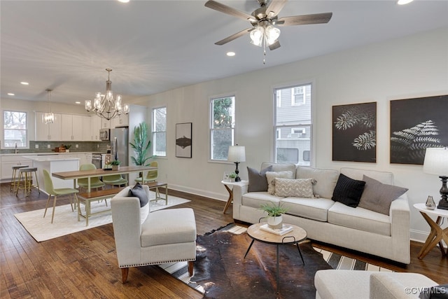 living room featuring ceiling fan with notable chandelier, plenty of natural light, baseboards, and dark wood-style flooring