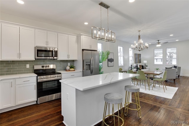 kitchen featuring tasteful backsplash, open floor plan, stainless steel appliances, a breakfast bar area, and white cabinets